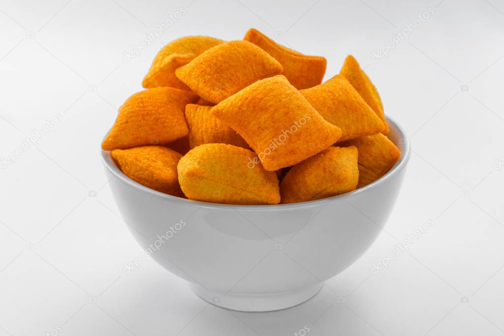 Orange corn chips in the form of pillows lie in a white bowl