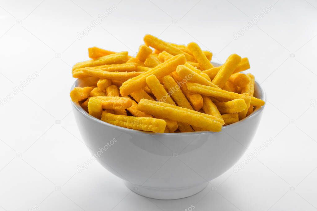 Yellow corn chips in the form of sticks lie in a white bowl