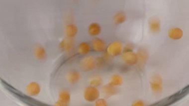 Camdan şeffaf bir kaseye düşen kuru sarı bezelyeler, yakın plan.