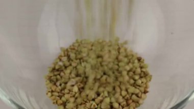 Yeşil karabuğday taneleri cam şeffaf bir kaseye düşer, yakın plan.