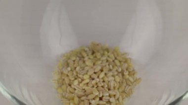 Şeffaf cam bir kâseye dökülen inci arpa taneleri, yakın plan.