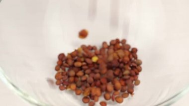 Kahverengi mercimekler cam şeffaf bir kaseye dökülüyor, yakın plan.