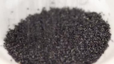 Haşhaş tohumları cam şeffaf bir kaseye düşer. Yakın plan.