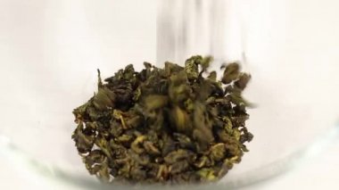 Oolong yeşil çay yaprakları şeffaf cam bir kaseye düşer, yakın plan.