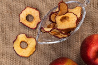 Gri arka planda cam bir kasede kırmızı elma cipsi.