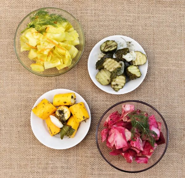 Yapraklı mayalanmış kabak, zerdeçal ve havuçlu lahana, sarımsaklı salatalık ve pancar dilimlenmiş lahana ve çuval bezinin arka planında ayrı tabaklarda dereotu.