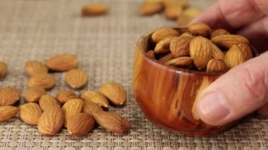 Bir adamın eli gri bir hasır yüzeye bademli kahverengi bir tahta kase koyar.