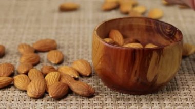 Erkek eli bademleri kahverengi tahta bir kaseye doldurur, yakın plan.
