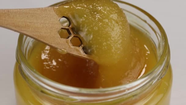 一个有蜂窝状小孔的木制勺子在一个装有深色蜂蜜的玻璃瓶中旋转 这是一个特写 — 图库视频影像