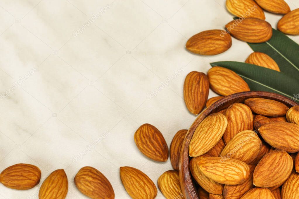 Almond nuts lie in a brown wooden bowl and on white marble, close-up