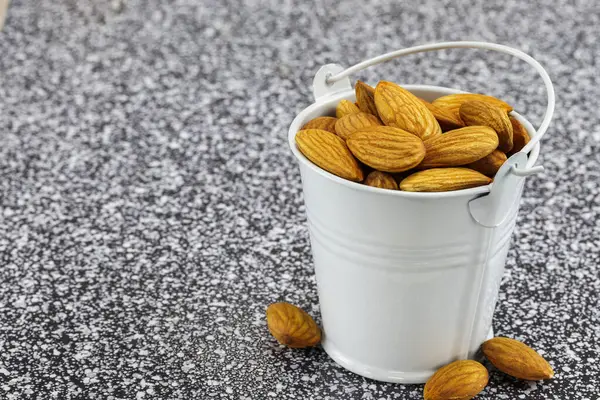 Badem ceviziyle dolu beyaz metal bir kova siyah beyaz mermer üzerinde duruyor.