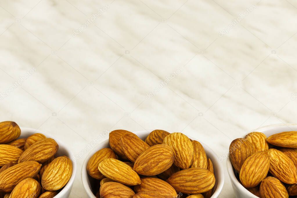 Three white bowls with almonds stand on a white marble surface, close-up