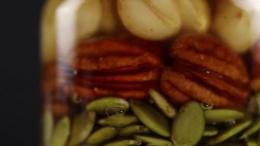 Balın içinde fındık ve kabak tohumlarının karışımı olan iki cam kavanoz saat yönünde döner, yan görünüm, çok yakın plan