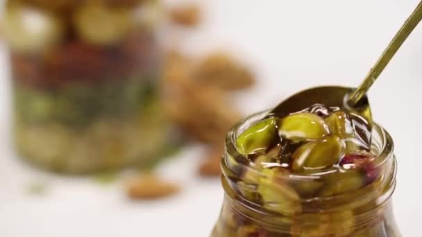 从一个盛满蜂蜜和坚果的玻璃瓶里拿出一只装有开心果的金属勺子 — 图库视频影像