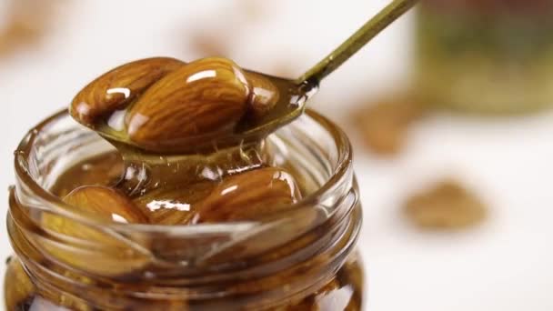 蜂蜜とナッツで満たされたガラス瓶から蜂蜜のアーモンドと金属スプーンを取り出した — ストック動画