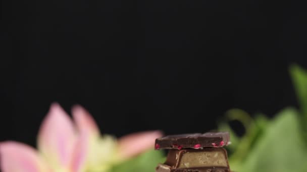 Pyramide de morceaux de chocolat noir avec différentes garnitures sur une feuille sur un fond de fleurs 