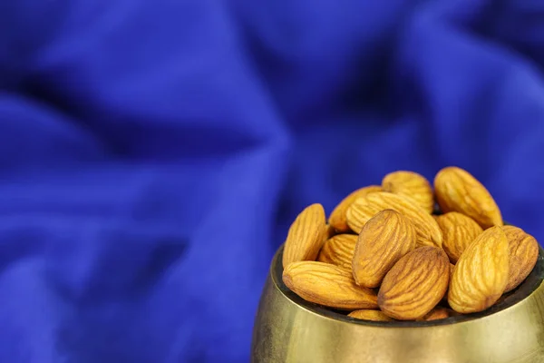 Almonds in a brass bowl on a blue background, close-up