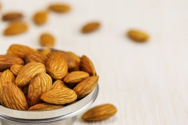 Bademler metal bir kasede ve beyaz bir yüzeyde, yakın plan.