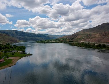 Beebe Köprüsü Parkı 'nın açık mavi gökyüzü ve parlak kümülüs bulutlarıyla Chelan Washington' ın dışındaki Columbia Nehri ile sarp bir dağ ortamında kayda değer bir hava fotoğrafı..