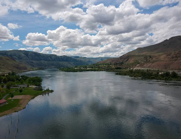 Beebe Köprüsü Parkı 'nın açık mavi gökyüzü ve parlak kümülüs bulutlarıyla Chelan Washington' ın dışındaki Columbia Nehri ile sarp bir dağ ortamında kayda değer bir hava fotoğrafı..