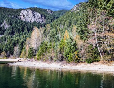 Emerald, Ross Gölü Ulusal Eğlence Bölgesi 'ni turuncu ve yeşil ağaçlarla donatmış. Dağlık bir arazide mavi gökyüzü ve sonbaharda bulutlar Washington eyaletindeki ulusal parkı kasıp kavuruyor.