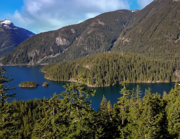 Emerald colored Ross Lake National recreation area with orange and green trees in a mountain landscape with a blue sky and clouds in the fall in the north cascades national park in washington state