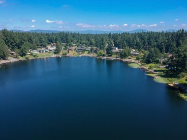Berrak bir yaz gününde, sakin gölgeli bir göl. Suya yansıyan ağaçlar, mavi bir gökyüzü ve Washington 'daki Renton King County limanında zambak kaplı beyaz bulutlar.