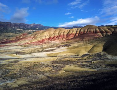 Breathing and colorful Painted Hills covered in red, tan, black, orange, and yellow stripes on a partly cloudy autumn day at the John Day Fossil Beds in Mitchell Oregon clipart