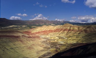 Mitchell Oregon 'daki John Day Fosil Yatakları' nda bulutlu bir sonbahar gününde kırmızı, bronzlaşmış, siyah, turuncu ve sarı çizgilerle kaplanmış renkli tepeler.