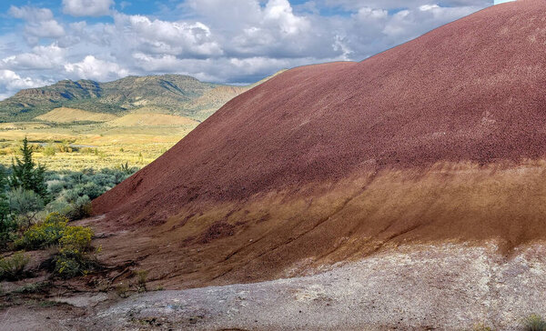 Захватывающие дух красочные красно-белые глиняные окаменелости с красивым полупустынным фоном с большими белыми облаками и голубым небом на тропе Джона Дэя ископаемых в бухте в Орегоне
