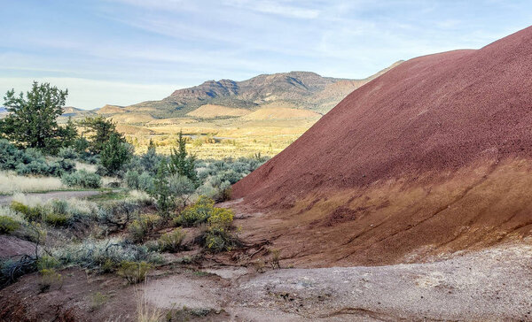 Захватывающие дух красочные красно-белые глиняные окаменелости с красивым полупустынным фоном с большими белыми облаками и голубым небом на тропе Джона Дэя ископаемых в бухте в Орегоне
