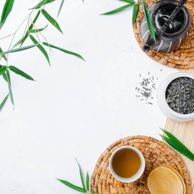Çay fincanında yeşil çay ve bambu yapraklı beyaz masada siyah çaydanlık. .