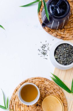 Çay fincanında yeşil çay ve bambu yapraklı beyaz masada siyah çaydanlık. .