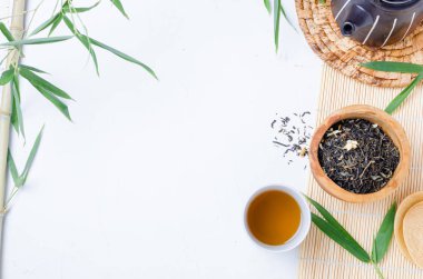 Çay fincanında yeşil çay ve bambu yapraklı beyaz masada siyah çaydanlık. .