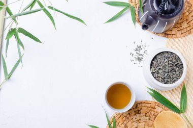 Çay fincanında yeşil çay ve bambu yapraklı beyaz masada siyah çaydanlık. .