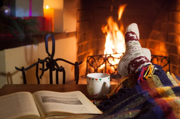 Man and woman in warm socks near the fireplace. Cup with a hot drink. Heart.