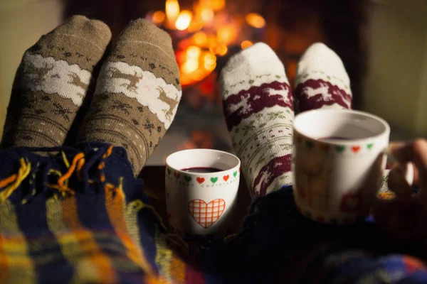 Man and woman in warm socks near the fireplace. Cup with a hot drink. Heart.