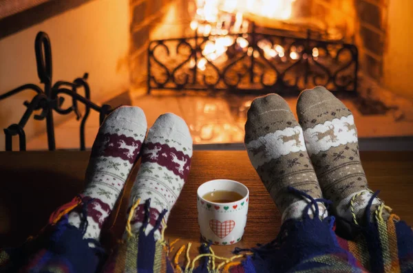 Man and woman in warm socks near the fireplace. Cup with a hot drink. Heart.