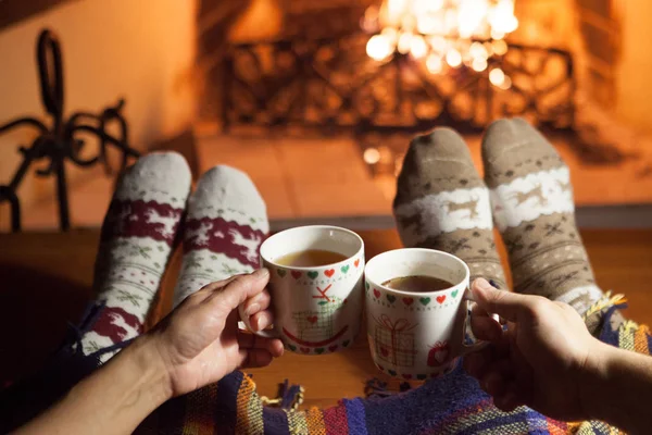 Man and woman in warm socks near the fireplace. Cup with a hot drink. Heart.