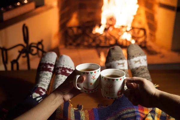 Man and woman in warm socks near the fireplace. Cup with a hot drink. Heart.