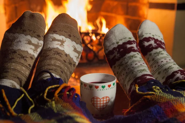 Şöminenin yanındaki sıcak çoraplı kadın ve erkek. Sıcak bir bardakla. Kalp.
