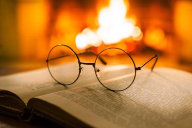 Açık antik bir kitap, antika bardaklar ve şöminenin önünde bir fincan sıcak içecek. Akşam masalları. Fantezi.