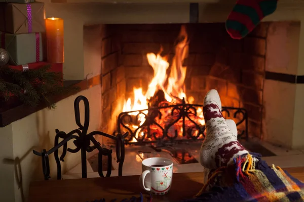 Man and woman in warm socks near the fireplace. Cup with a hot drink. Heart.