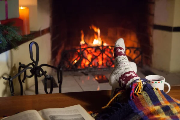 Man and woman in warm socks near the fireplace. Cup with a hot drink. Heart.