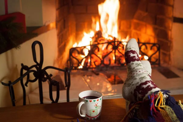 Man and woman in warm socks near the fireplace. Cup with a hot drink. Heart.