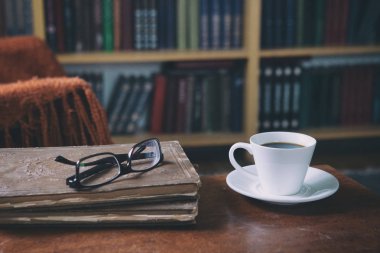 Kitaplar ve bir fincan kahveyle rahatlama anları. Koltukta kedisi olan bir adam. Eski kitaplar, gözlükler, kütüphane..