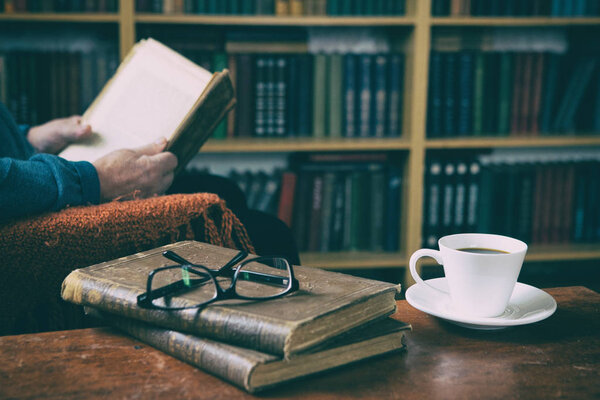 Sweet moments of relaxation with books and a cup of coffee. A man in an armchair with a cat. Vintage books, glasses, library.