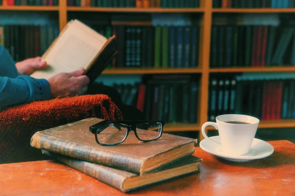 Kitaplar ve bir fincan kahveyle rahatlama anları. Koltukta kedisi olan bir adam. Eski kitaplar, gözlükler, kütüphane..