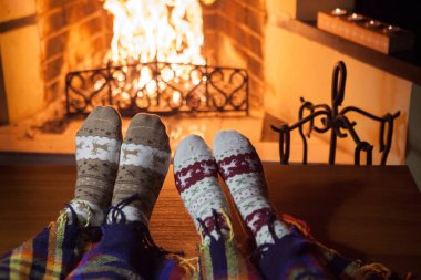 Kadın ve erkek, şöminenin önünde sıcak punç dolu çoraplar örüyorlar.