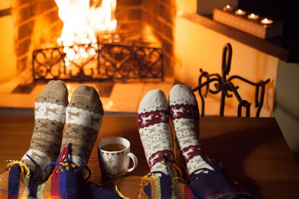Kadın ve erkek, şöminenin önünde sıcak punç dolu çoraplar örüyorlar.